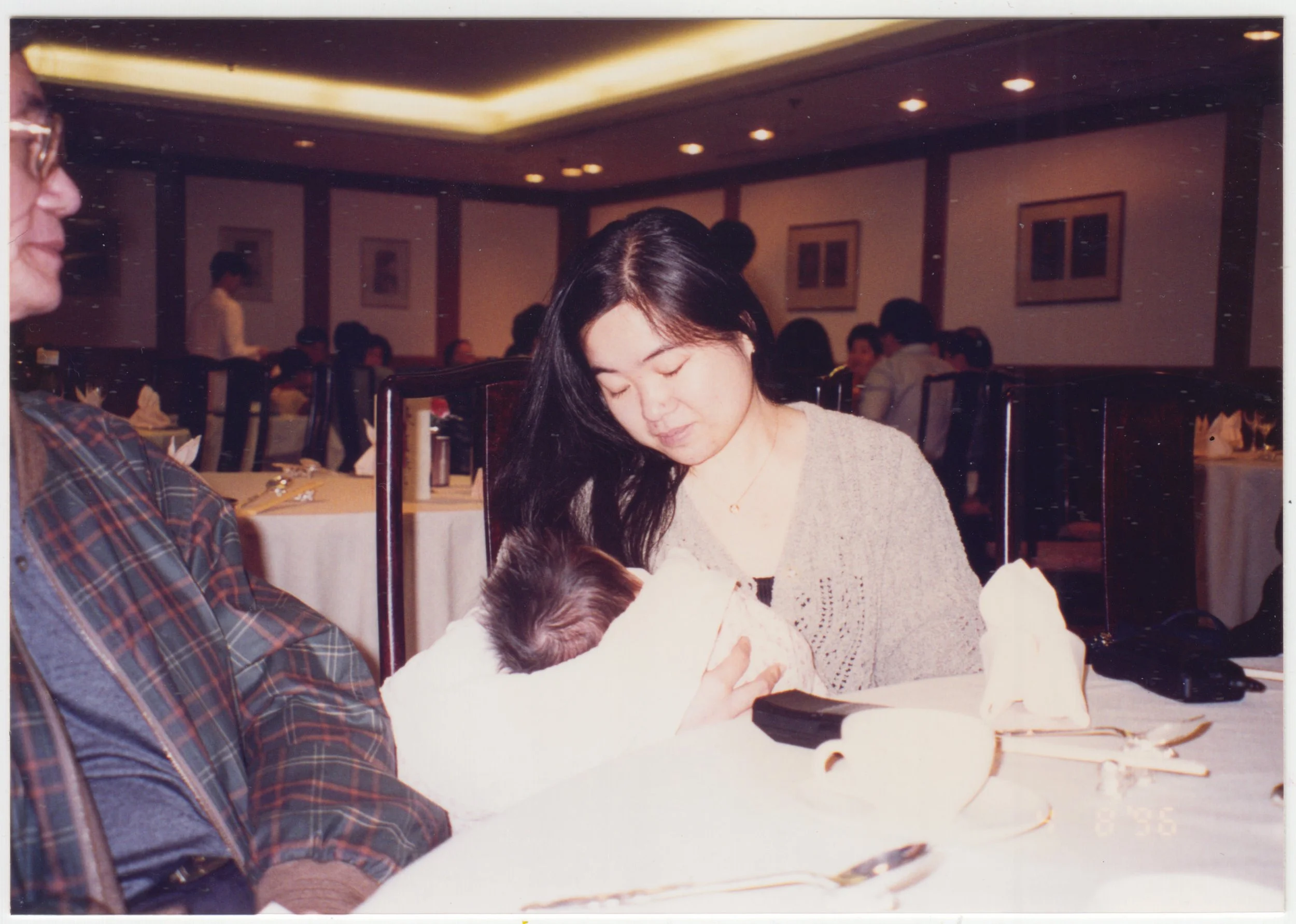 EE holding Charlotte at a family banquet while Grandpa watches. Taken on 8 April 1996.