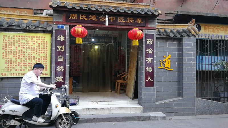 A blind, albino Taoist disciple sitting on a scooter enjoying a cigarette.