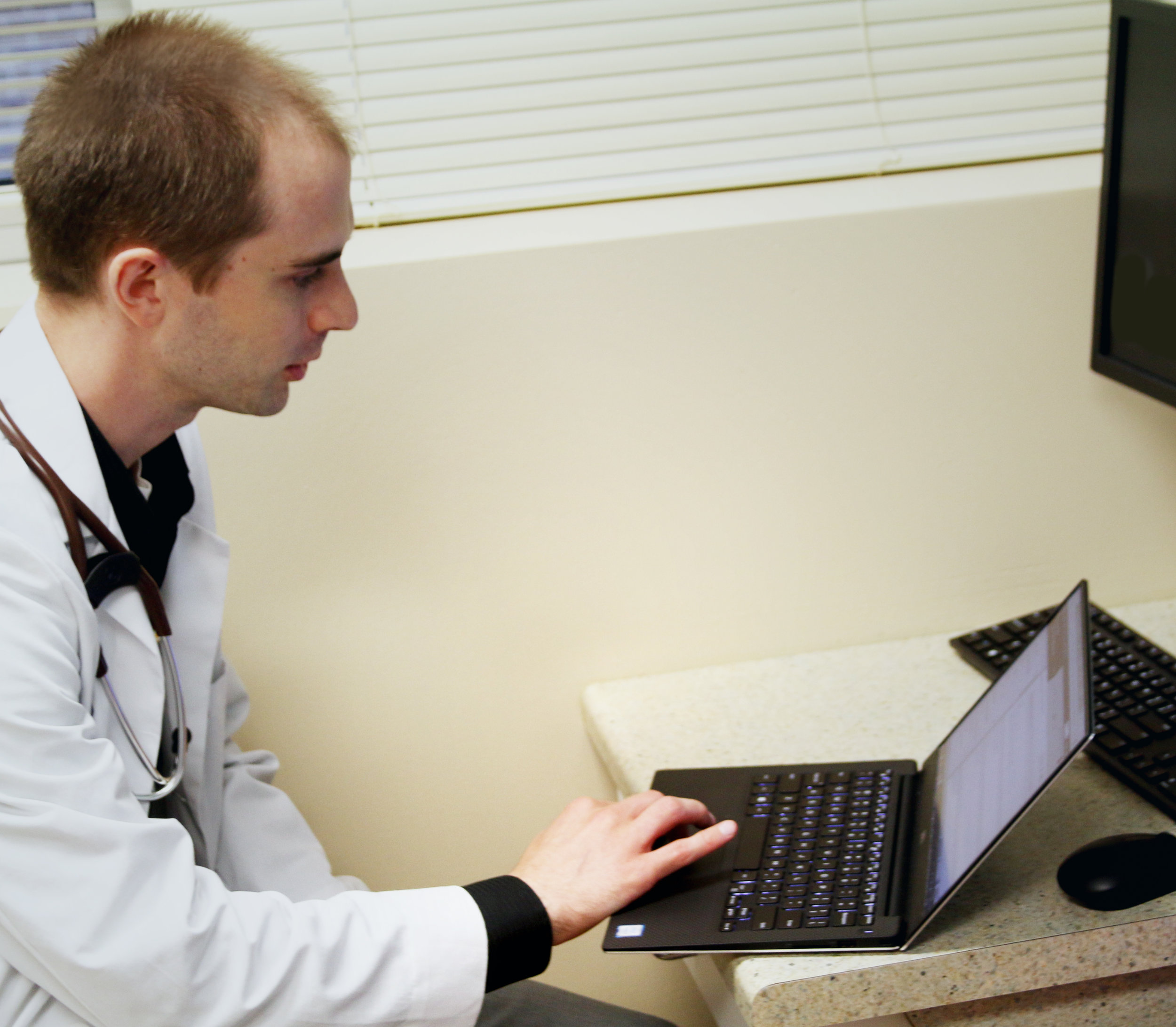 Doctor in white coat on laptop in front of desktop computer