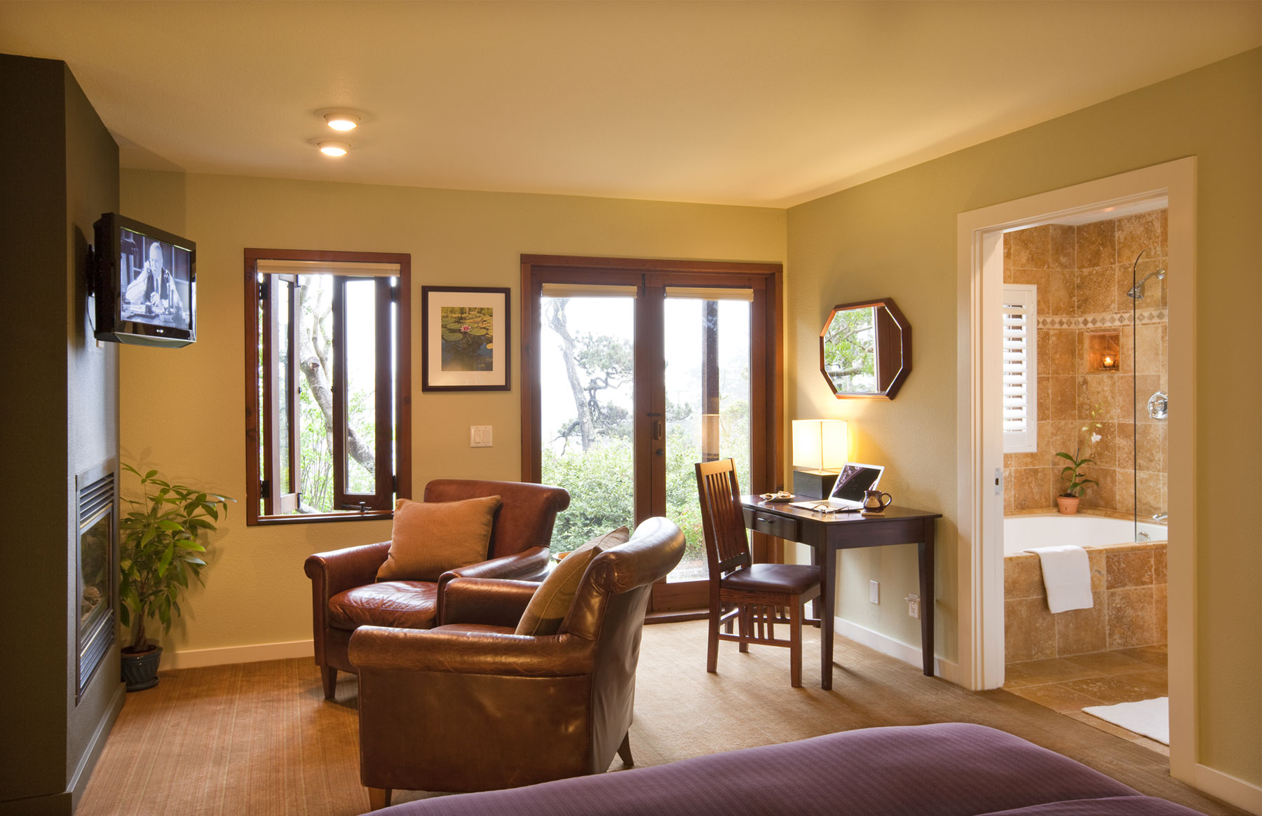 The Pine room with leather chairs in front of fireplace and flat screen TV, desk, French Doors, and tiled bathroom