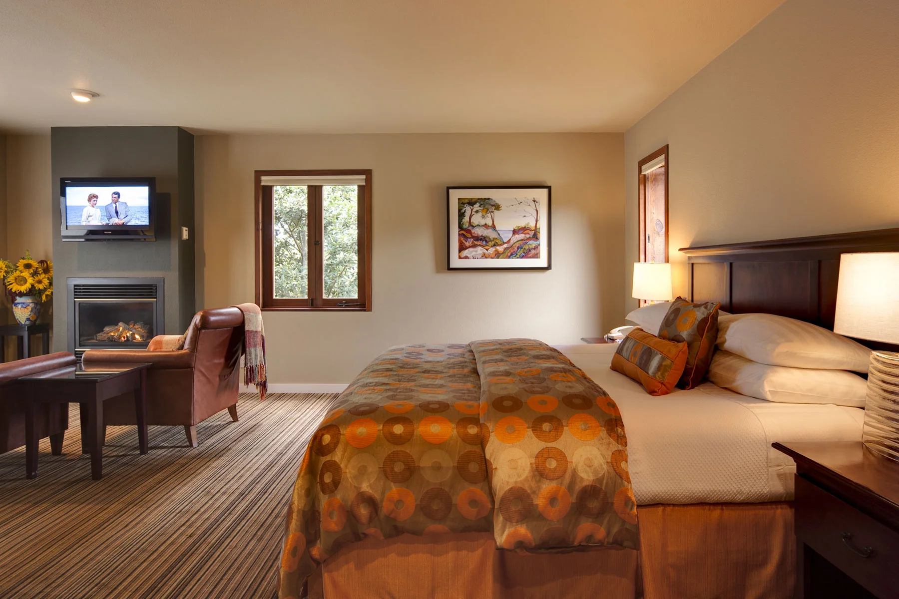 A room at the inn with a neatly made king bed, flat screen TV and fireplace.