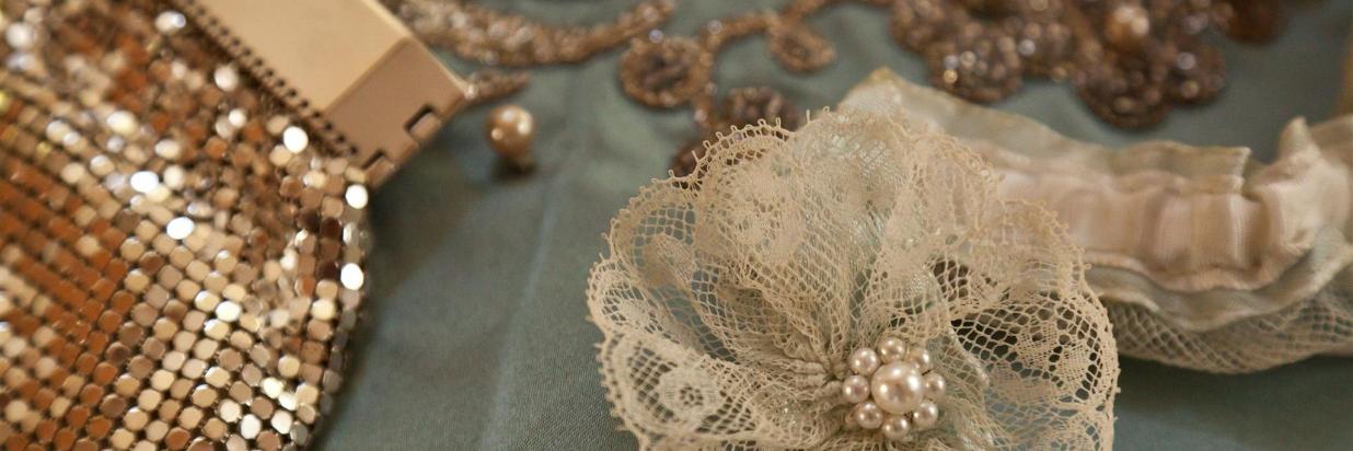 A close up of a shimmery purse, a lace and pearl hair accessory, and jewelry.