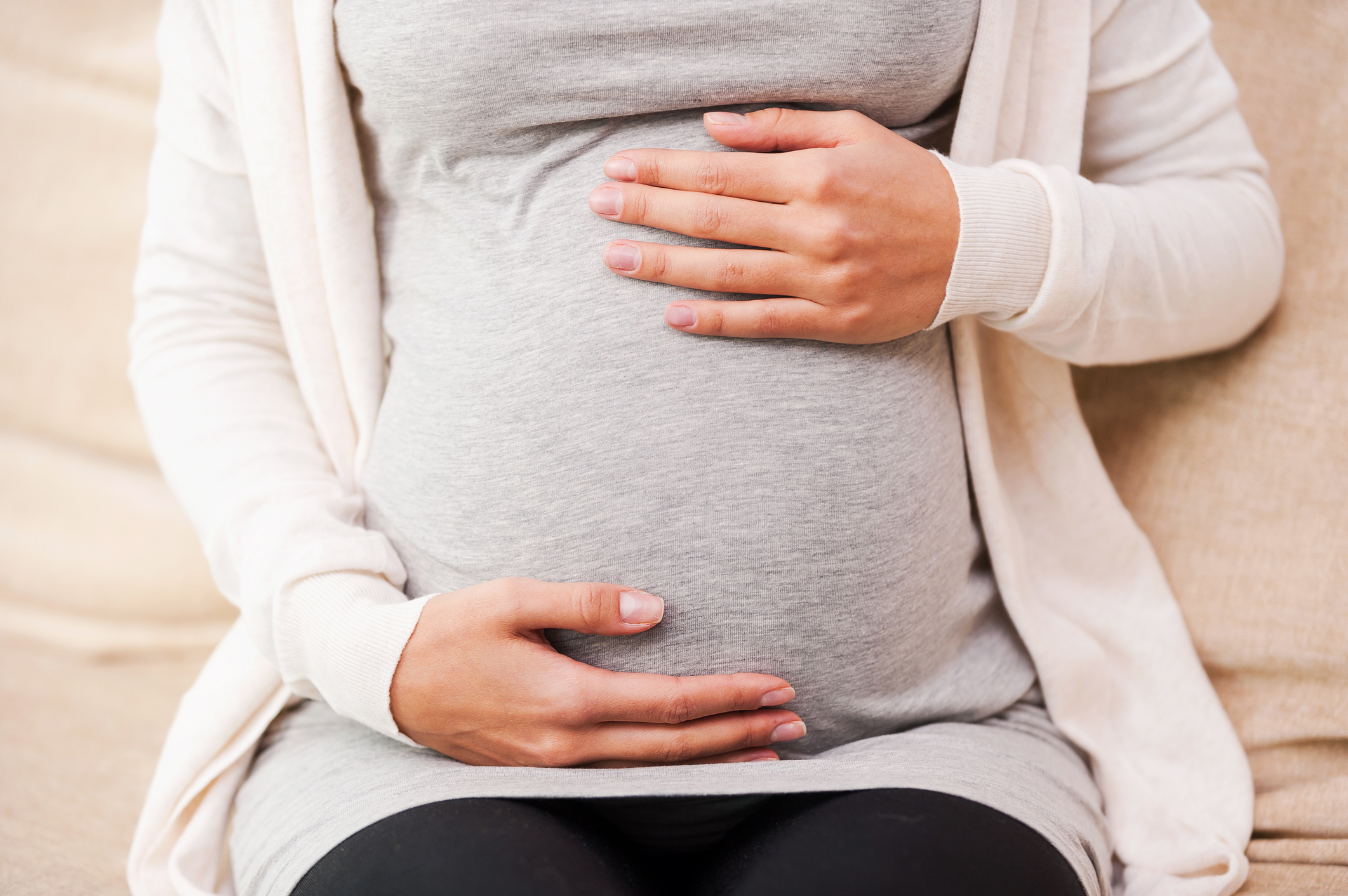 a close up of a woman’s pregnant belly with hands resting above and beneath it