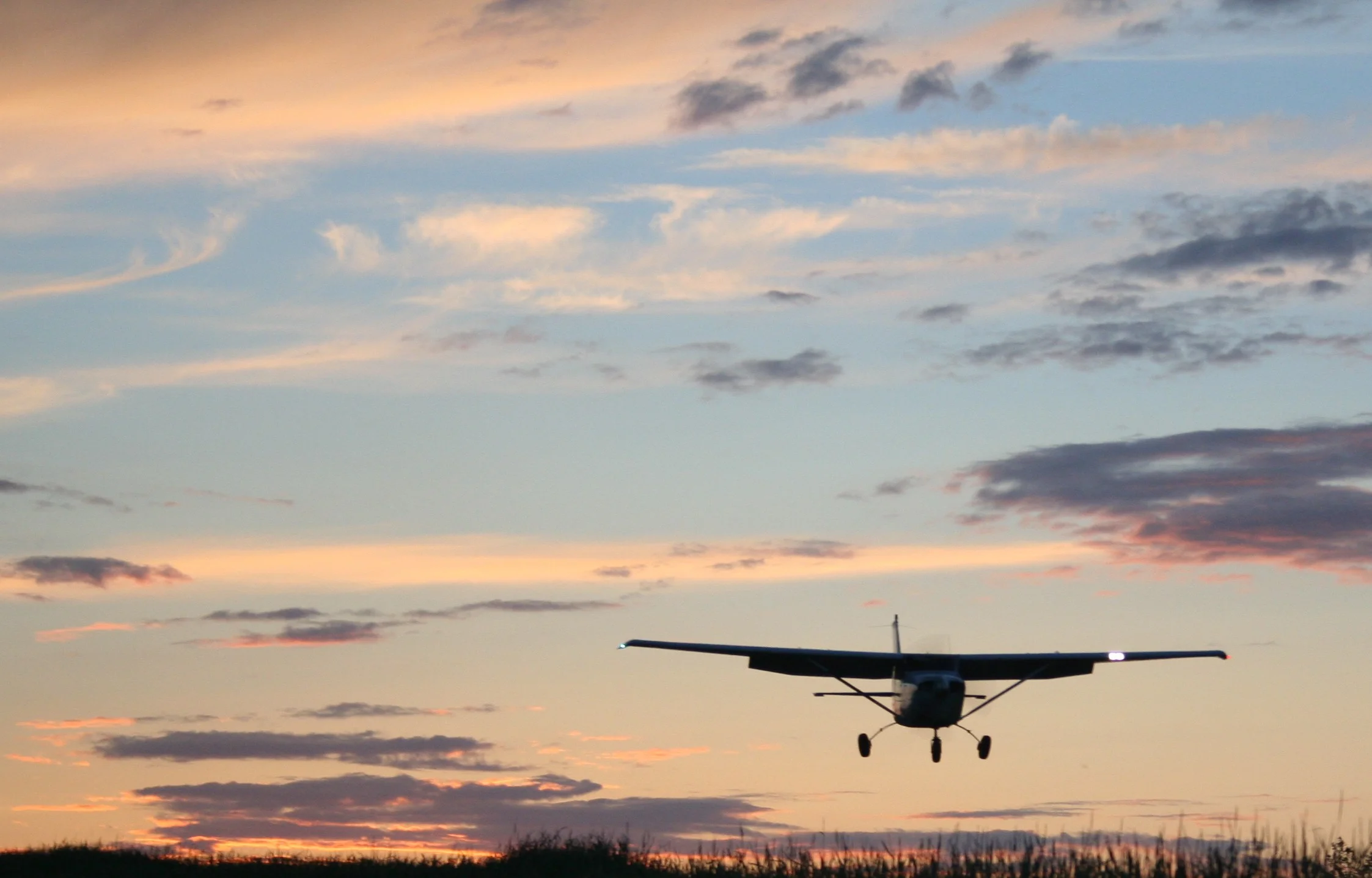A small plane landing with a sunset streaked sky behind it.