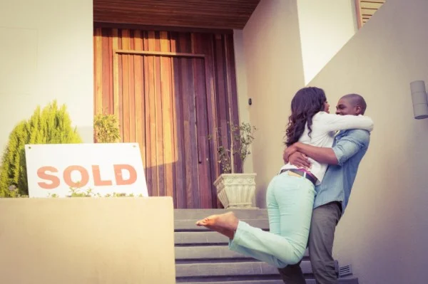 photo of a hugging young couple in front of a home with a sold sign
