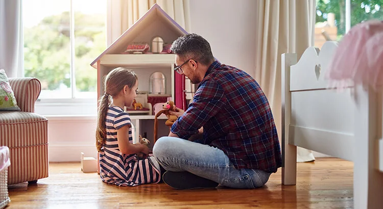 father and daughter playing with dollhouse in bedroom