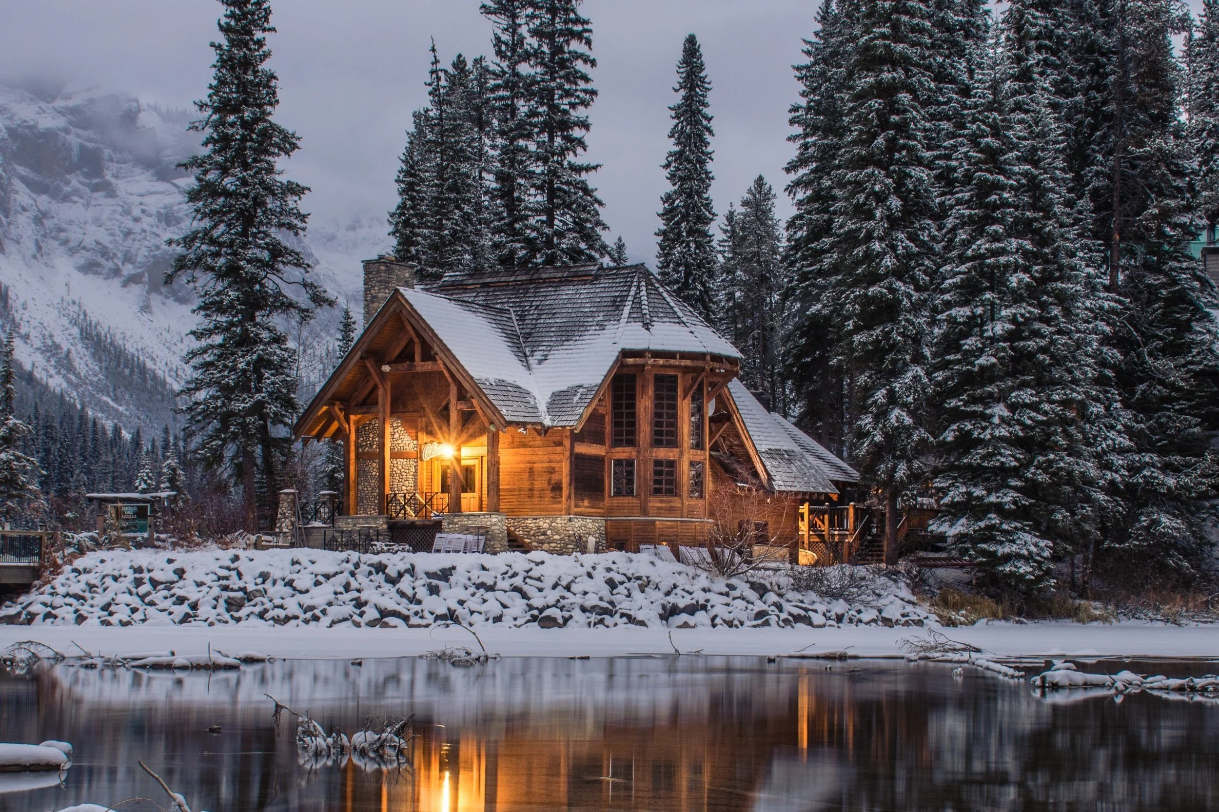photo of home covered with snow near a lake at twilight
