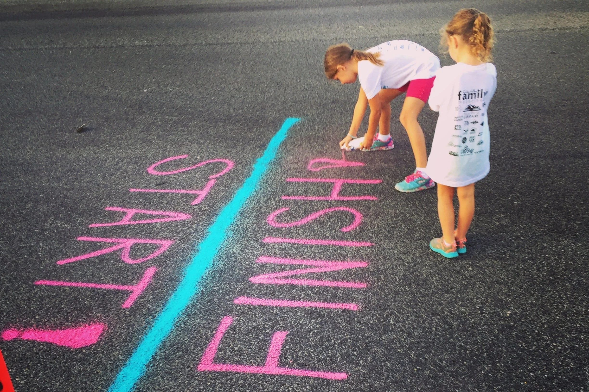 two young girls spray painting start and finish on asphalt
