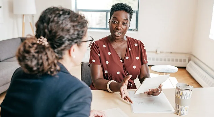 two women talking over a kitchen table with papers