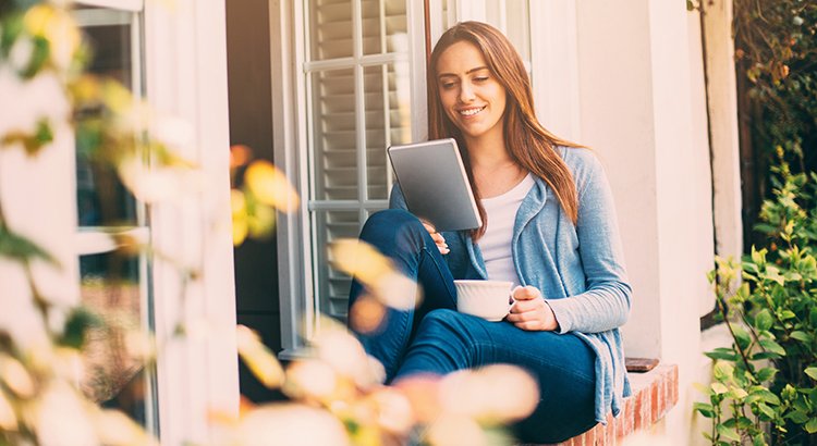 young woman looking at a notebook while reading by a home
