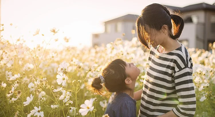 mother and daughter in front of flowers and home