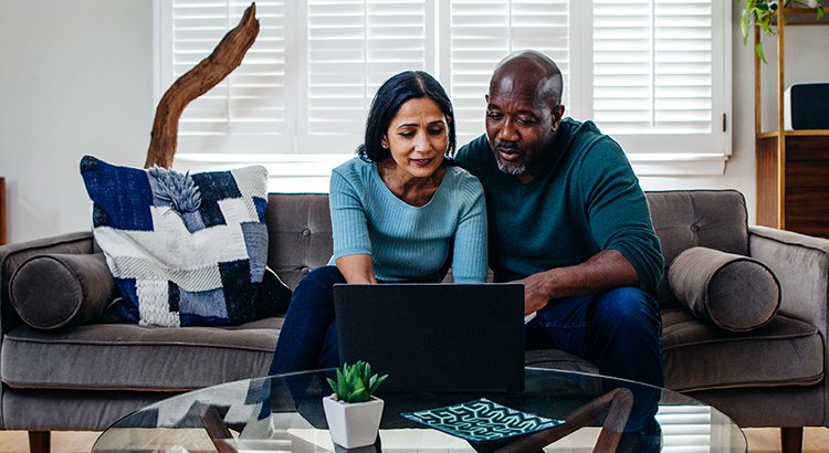 a man and woman sitting on their couch looking at a computer