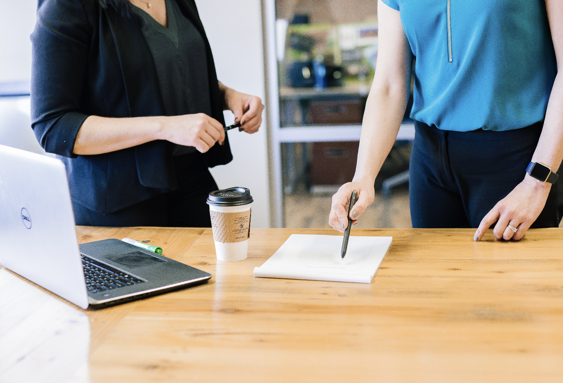 two people in front of desk, notepad and laptop
