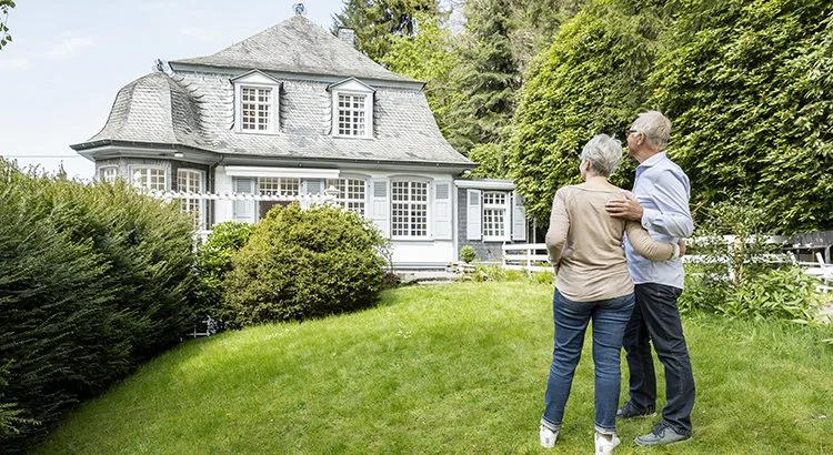 senior couple looking at home standing in front yard