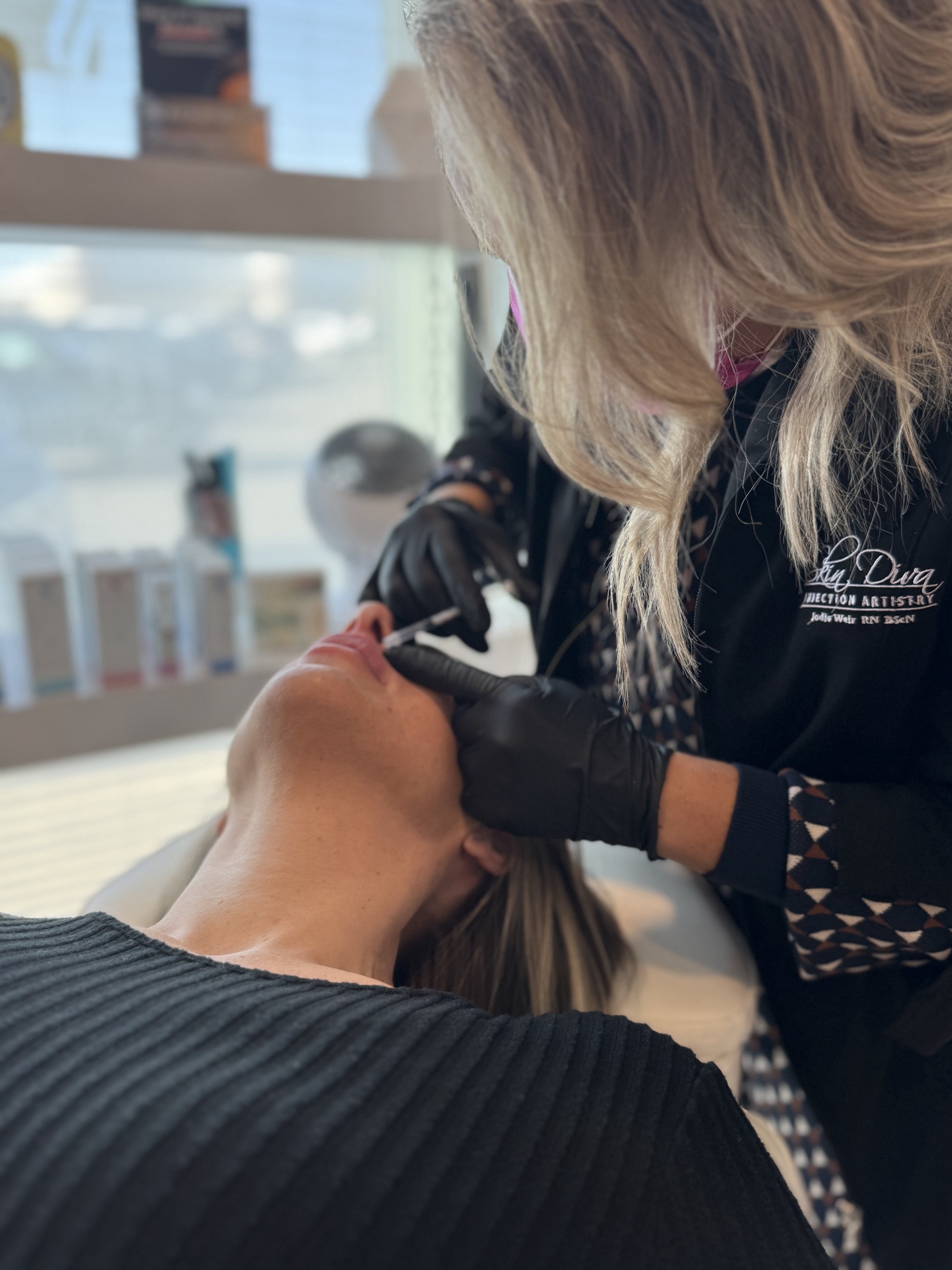 A healthcare professional administering lip injections injection to a woman's arm in a clinical setting.