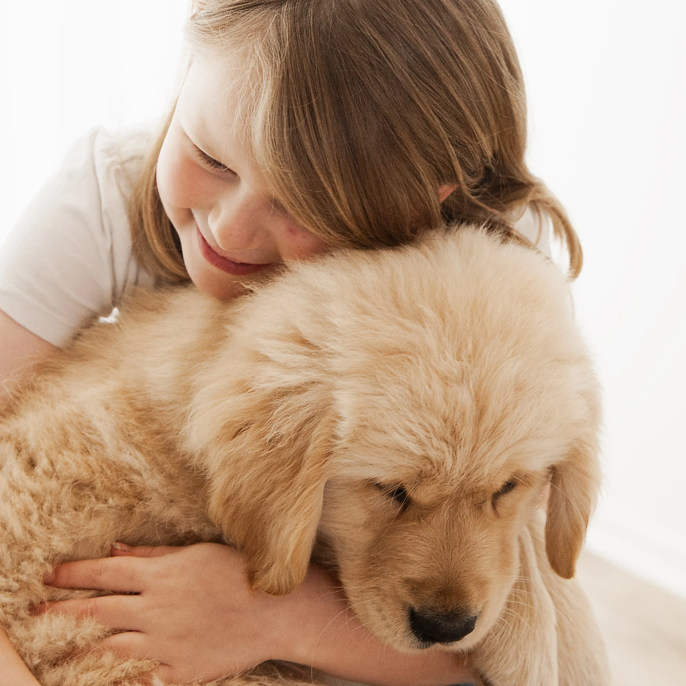 A young girl with brown hair hugging a golden retriever puppy