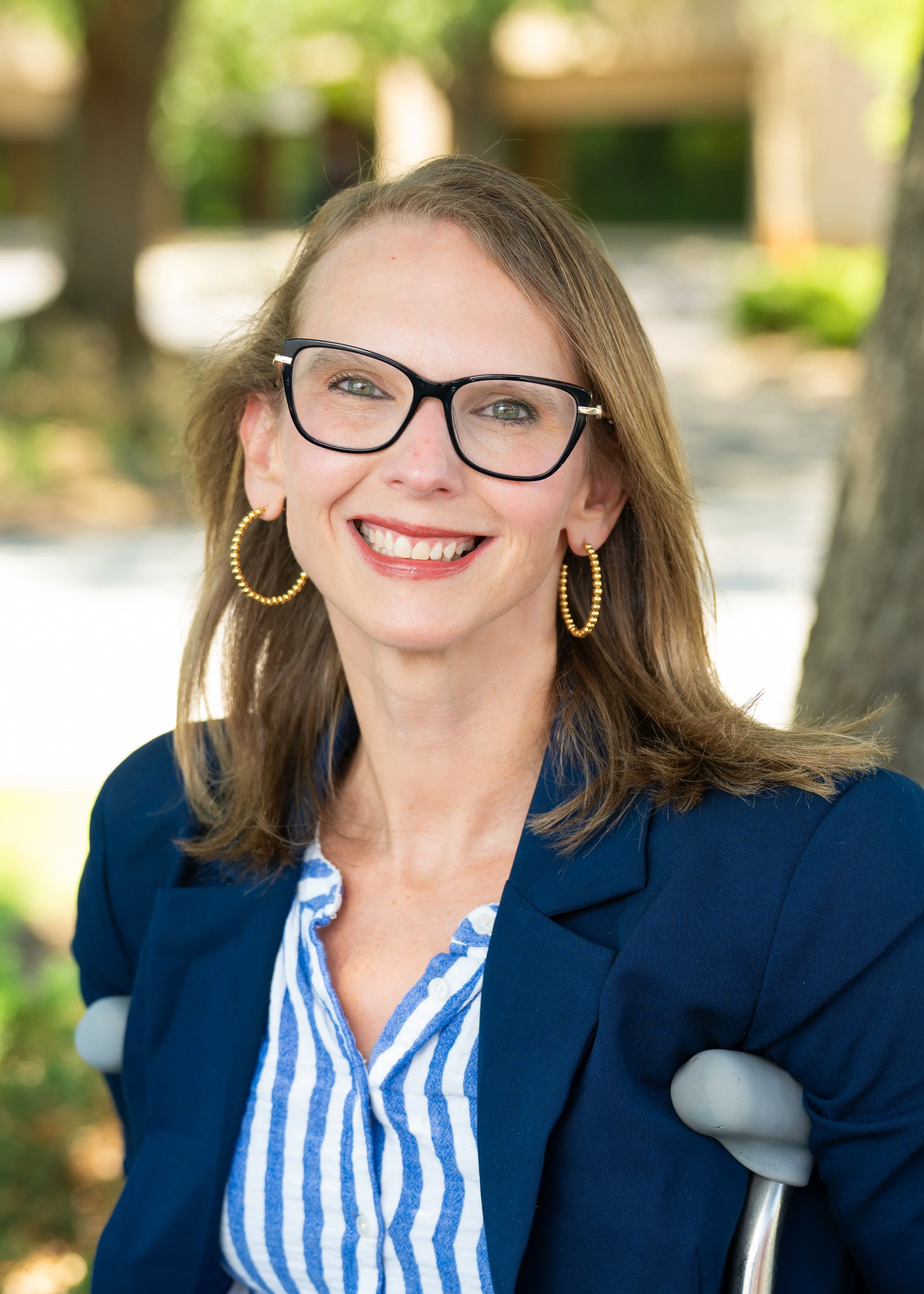 Kimberly, a white woman with glasses using crutches smiling outside.