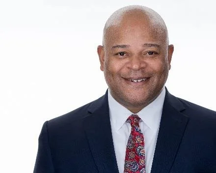Carlos, a man with brown skin and bald head wearing a suit and tie.