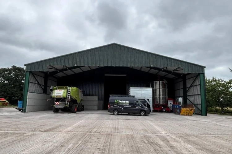 Steel-framed agricultural storage building with machinery and vehicles parked inside