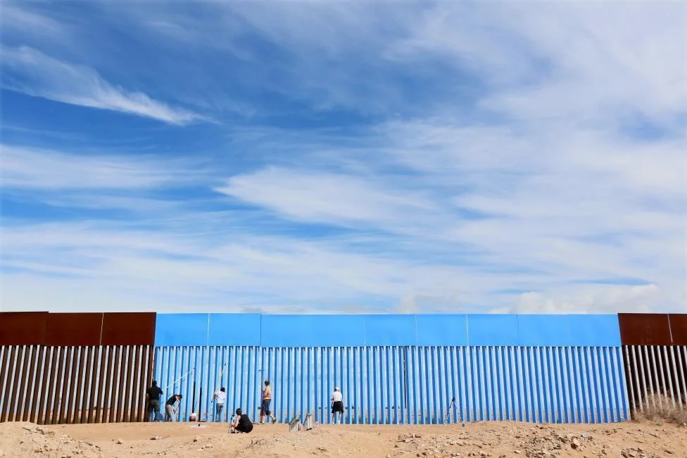 Volunteers paint the border fence between the United States and Mexico to give the illusion of transparency during the "Borrando la Frontera" (Erasing the Border) Art Project in Mexicali, Mexico. REUTERS/Sandy Huffaker