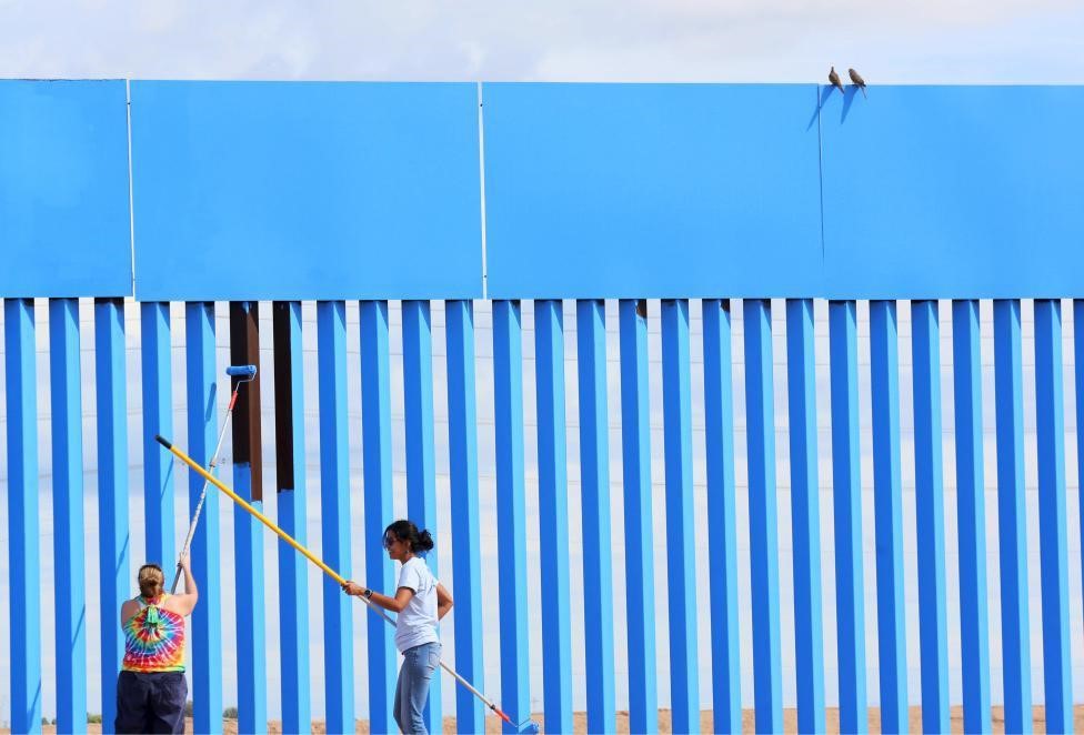 Volunteers Brooke Collins (L) and Ana Lucia Lopez paint the border fence, while two doves sit on top of the wall in Mexicali, Mexico. REUTERS/Sandy Huffaker