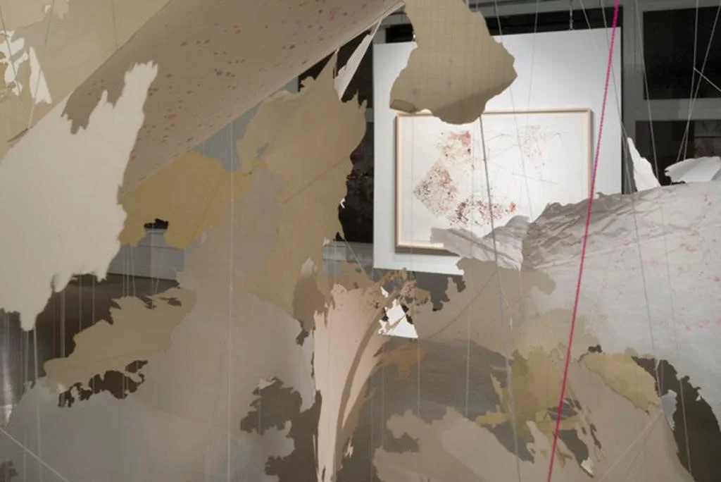 As in lacemaking, where patterns are made by removing threads from a woven background or by leaving empty spaces, Britton’sworksaremade by cutting through layers of collaged paper that are sometimes combined with underlying grid patterns. Her method resembles knot or lacemaking crafts conjoined with the nonlinear intelligence of spider webs. Her work’s decorative quality t the human hand, the singular beauty of craft.2 Her most recent project is an ambitious installation of 15 layered laminated glass panels measuring nearly 10 feet tall and 55 feet wide that will be installed at San Francisco International Airport this fall. Fabricated by Franz Mayer & Co. in Munich, Germany, this panoramic piece draws on research she did at the San Francisco Public Library about the construction of the airport, the landfill, the ghost coastlines, maps and plans of the area throughout its history, the populations traveling through, the weather patterns.