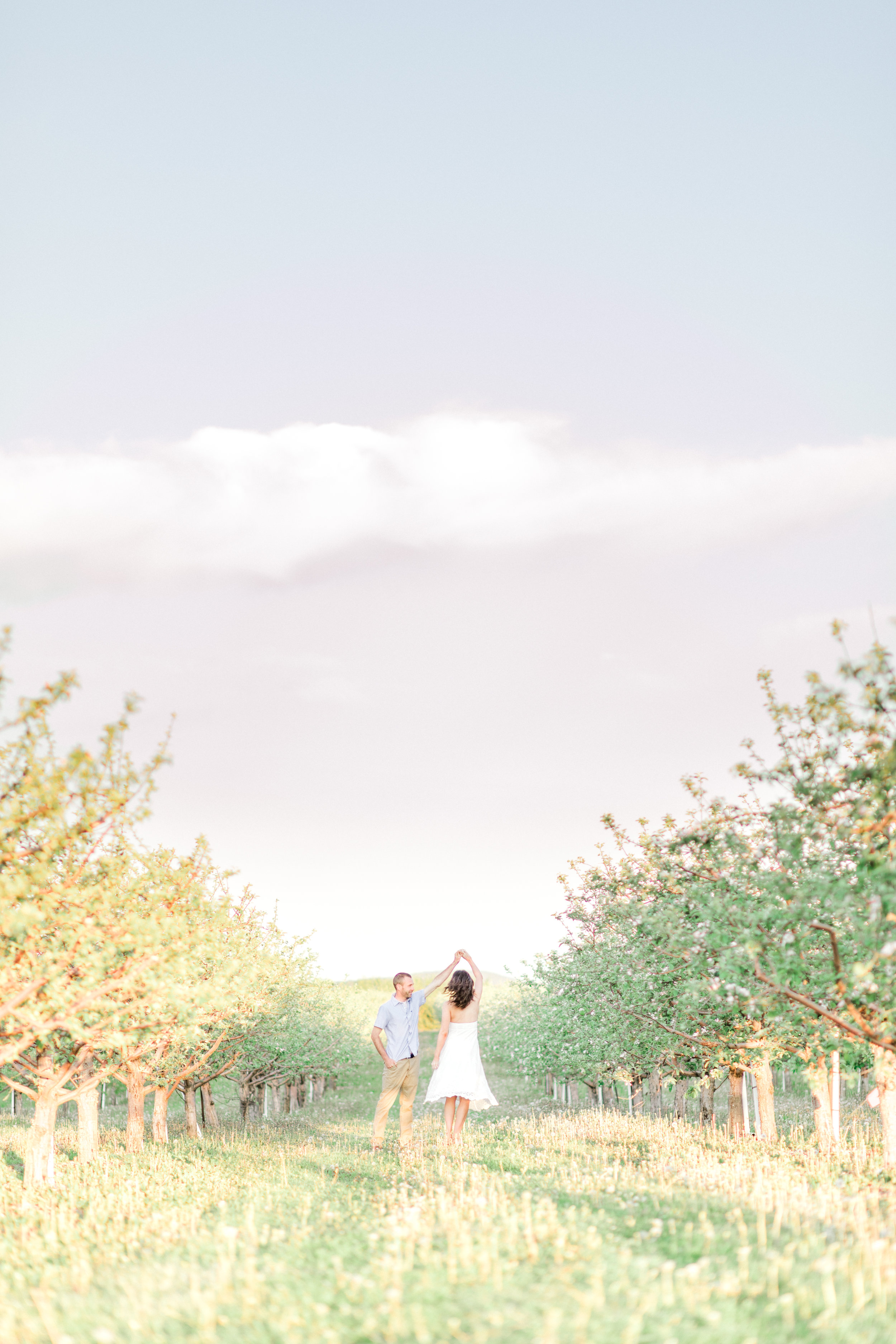 Engagement pictures should be romantic and fun! This golden glow session was jus that. Apple blossom engagement pictures in white dress for outfit ideas.Sunrise orchard engagement photo ideas with flower blossoms.