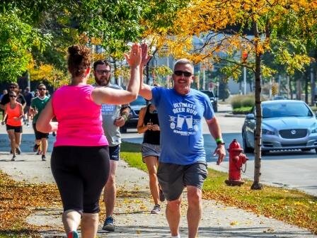  Two Ultimate Beer Run participants high five as they  run on a tree-lined street 