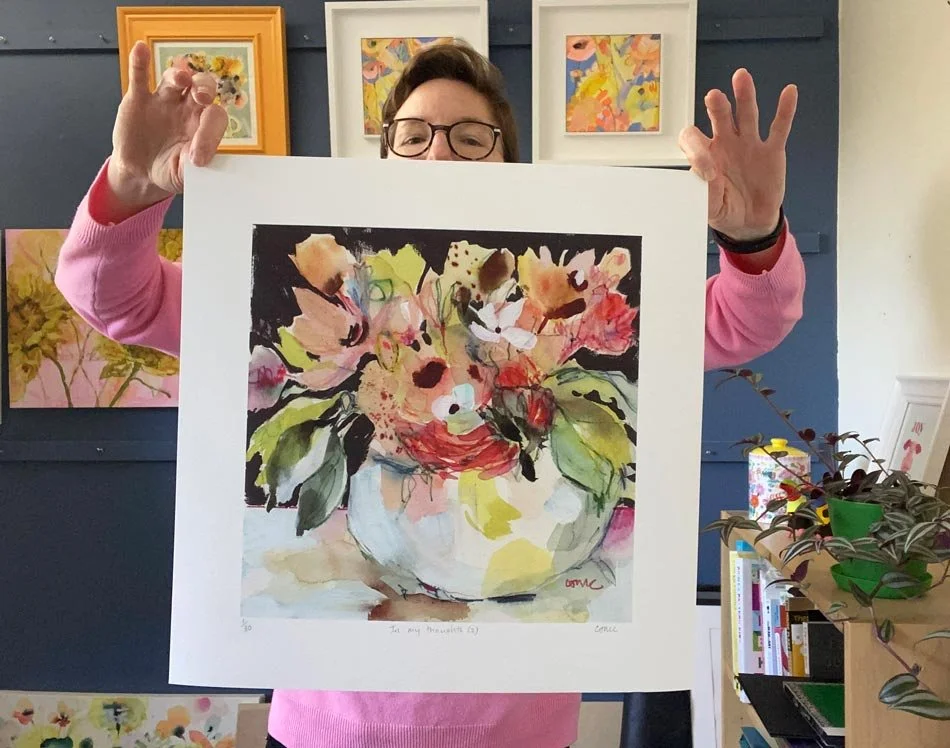 Artist Catherine Jennifer holding her Abundance floral Giclée print, featuring colourful flowers in a white vase.