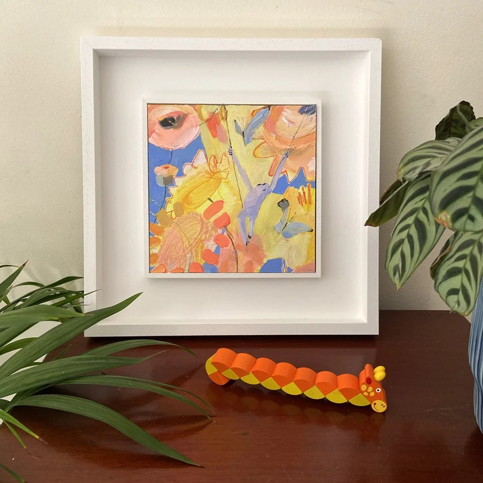 Nothing But Sky, original mixed-media painting by Catherine Jennifer photographed on a dark wooden cabinet with a colourful wooden snake ornament