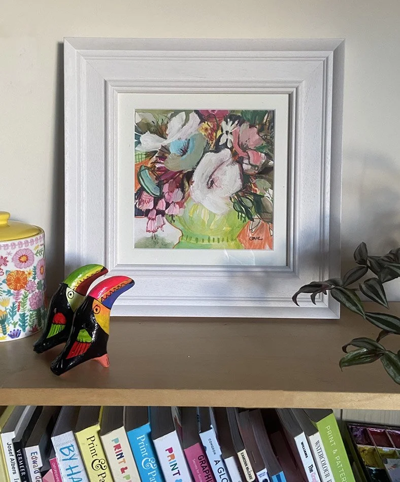 Flower Power — an expressive original floral painting by artist Catherine Jennifer, framed in a chunky white frame, and photographed on a shelf in the artist's studio