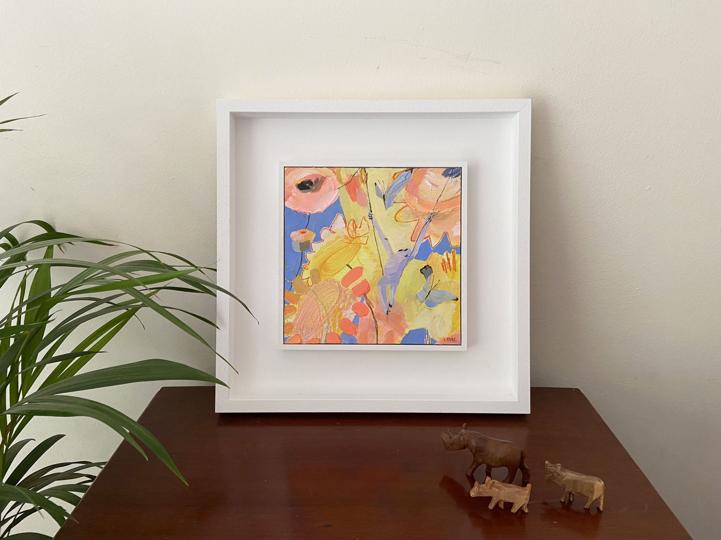 Nothing But Sky, original mixed-media painting by Catherine Jennifer photographed on a dark wooden cabinet with two wooden animal ornaments