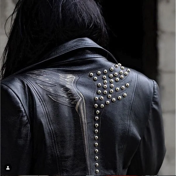 Back of a person wearing a black leather jacket with silver stud embellishments on the back.