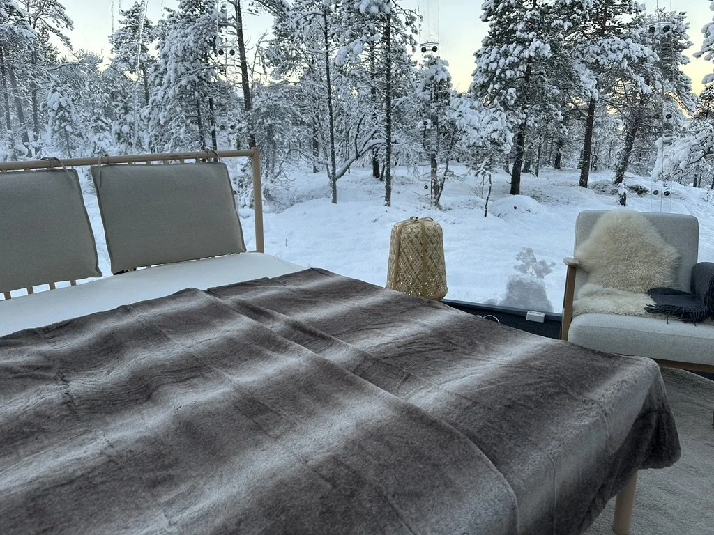 Warm seating inside ACIN's Aurora glass igloo surrounded by winter forest in Malangen