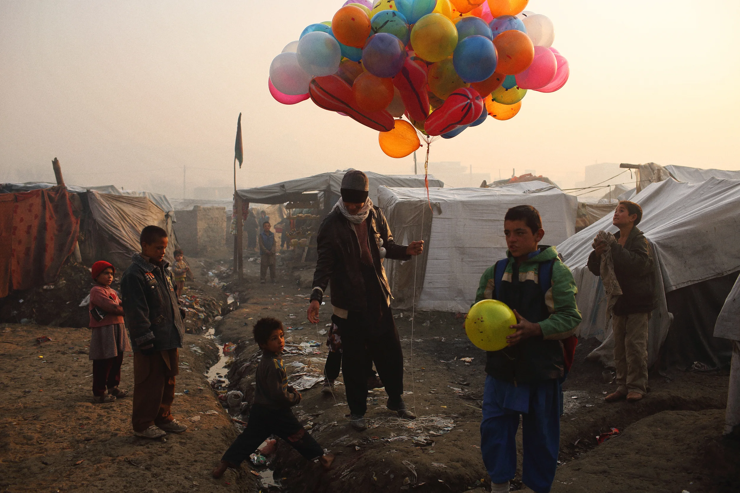  Even at sunrise in the dead of winter, a balloon-seller plies his trade in one of Kabul’s 50 informal settlements for displaced families. Kabul, December 2013 
