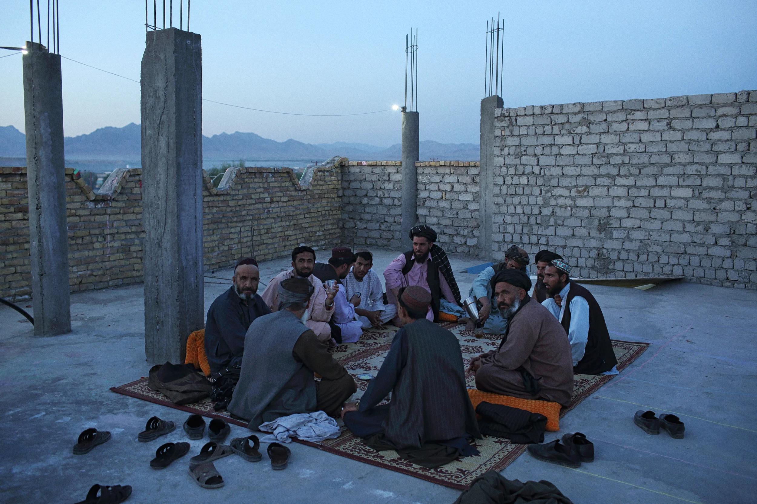 Men drink tea at dusk on the unfinished rooftop of a restaurant in Tarin Kot. Uruzgan Province, August, 2015. 
