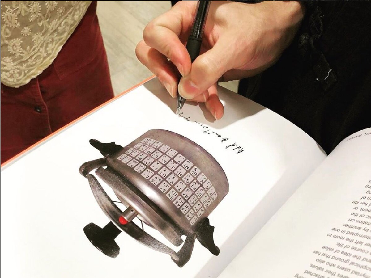 Adel Bentounsi signing the image of his artwork “C.V.” within the brochure to the group exhibition “Waiting for Omar Gatlato”.