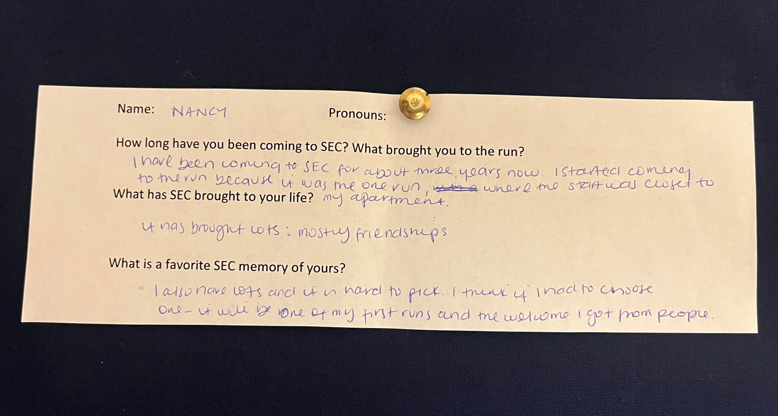 An image of a slip of paper with typed questions and hand written answers. The paper is pinned to a navy blue background with a gold metal thumbtack. The contents of the writing are written below the photo.