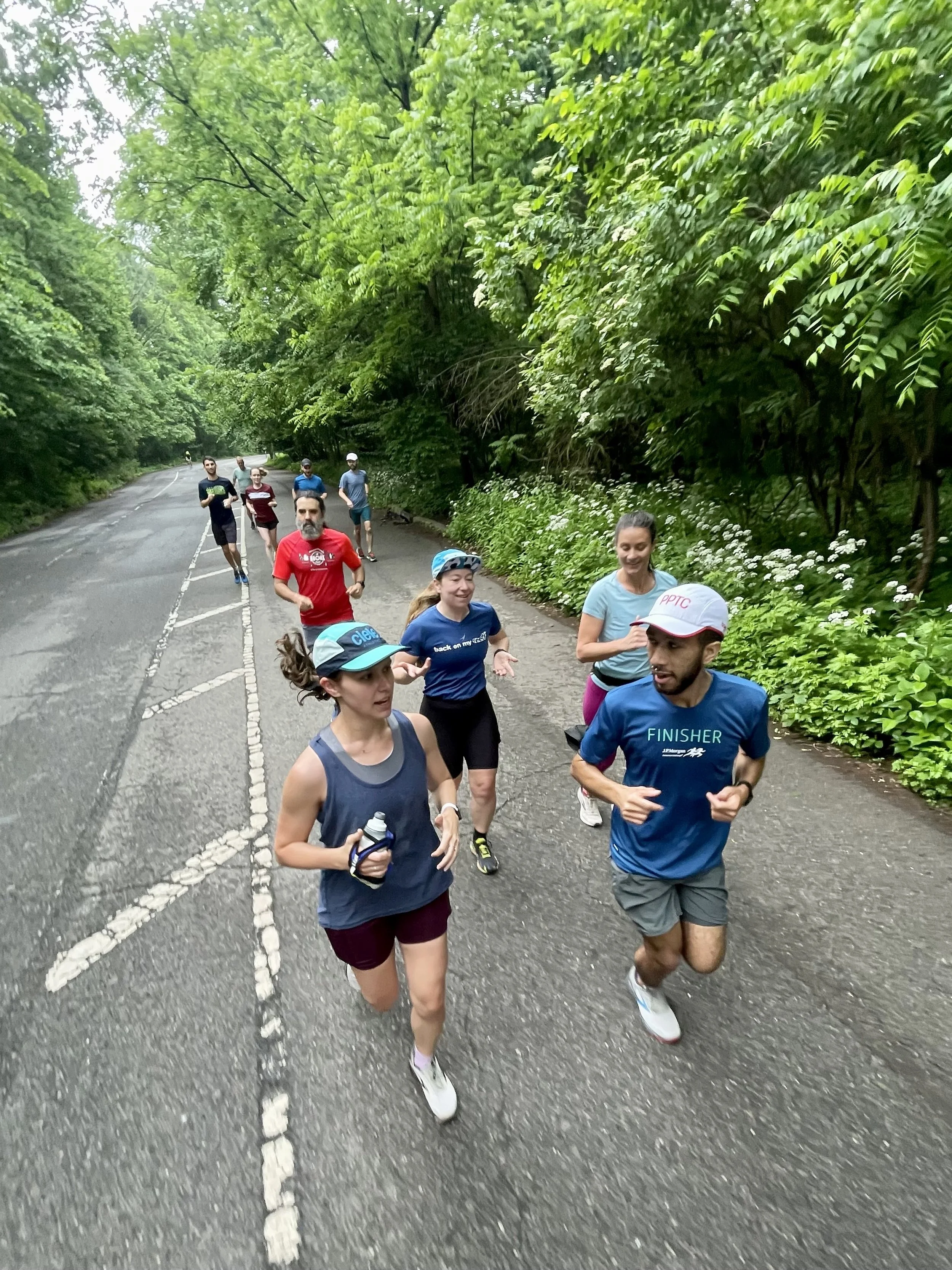 10 runners running on asphalt surrounded by verdant plant life. The runners are smiling and in mid conversation