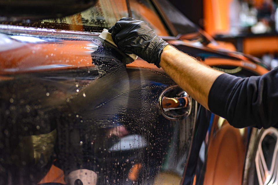  A hand polishing a orange body of a car  