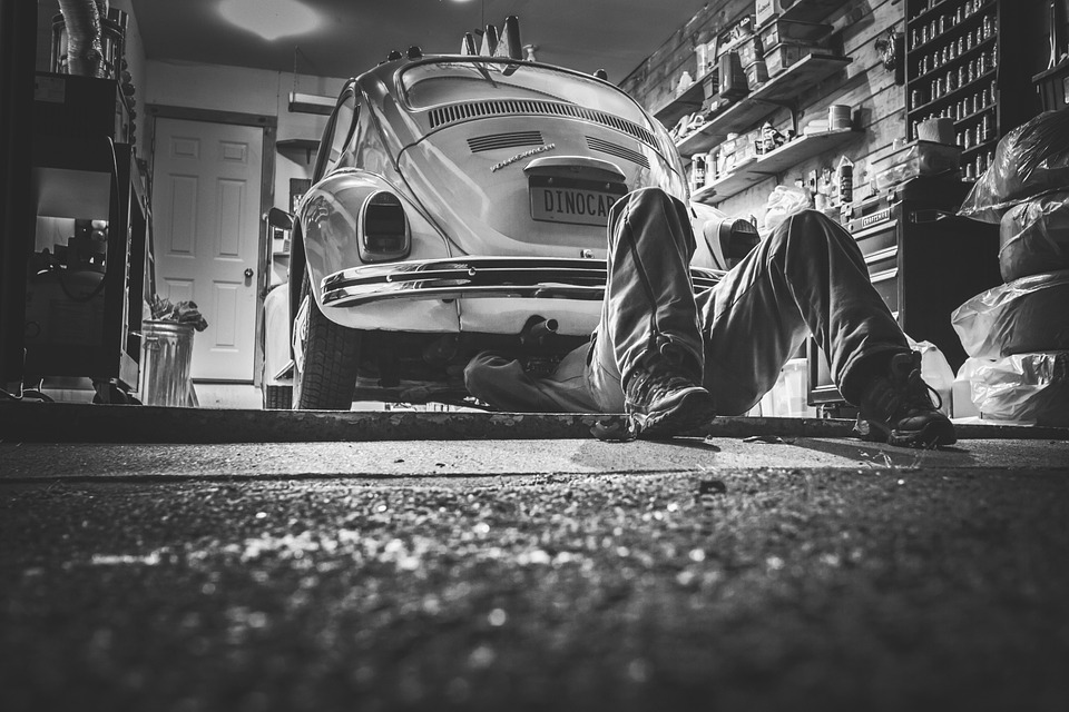  Black and white photo of a man underneath a old VW bug working on it  