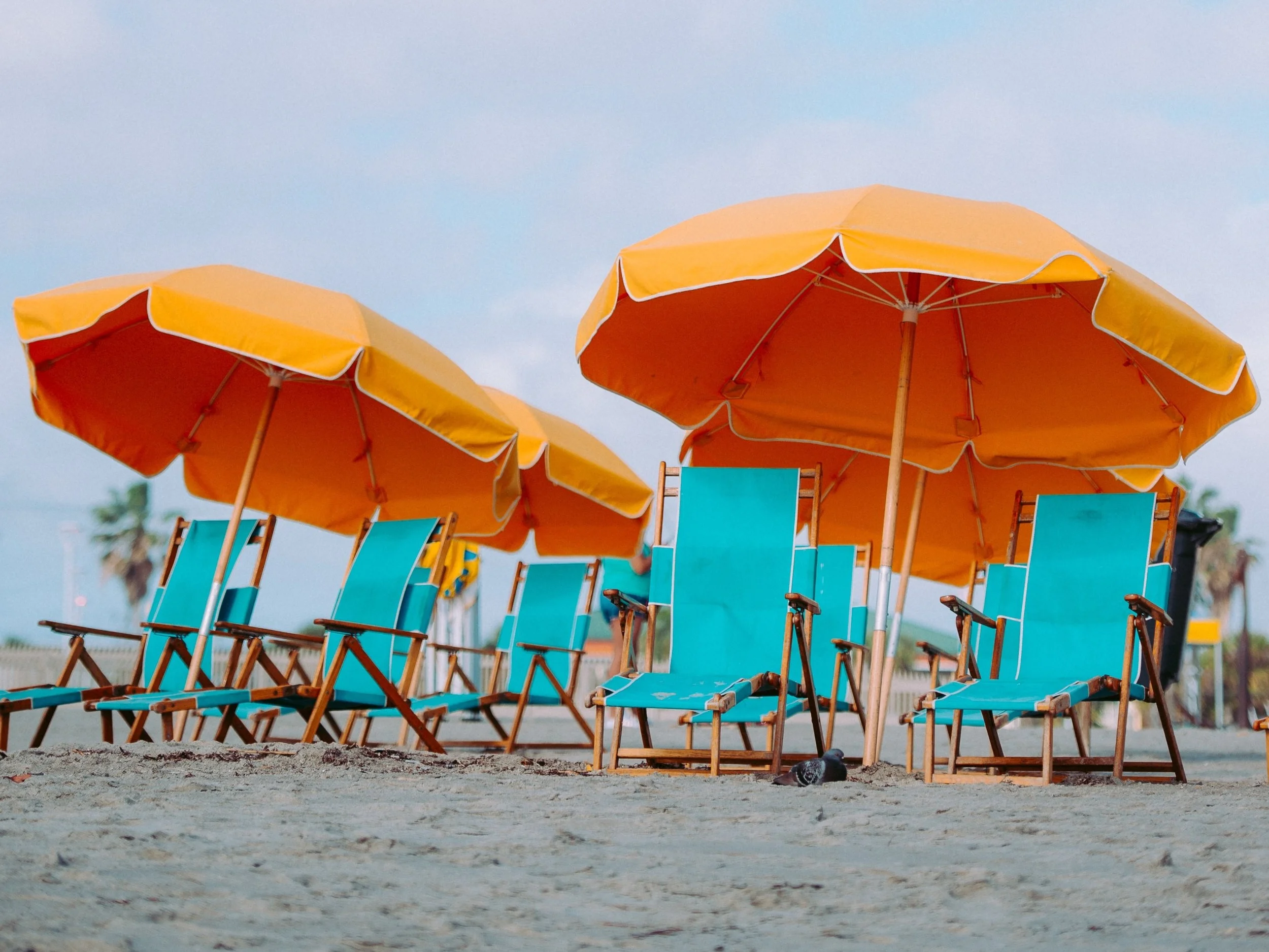 A beach setting with bright blue beach chairs shaded by bright yellow umbrellas