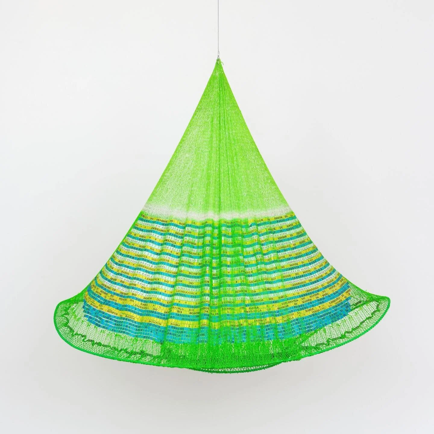 Carolina Caycedo, @lacaycedo 
Power to Fulfill Wishes or Bonfim, 2025, artisanal hand-dyed cast net, Bonfim ribbon, powder coated steel, lead weights, thread.

The Cosmotarrayas series comprises hanging sculptures that embody &ldquo;stories of dispos