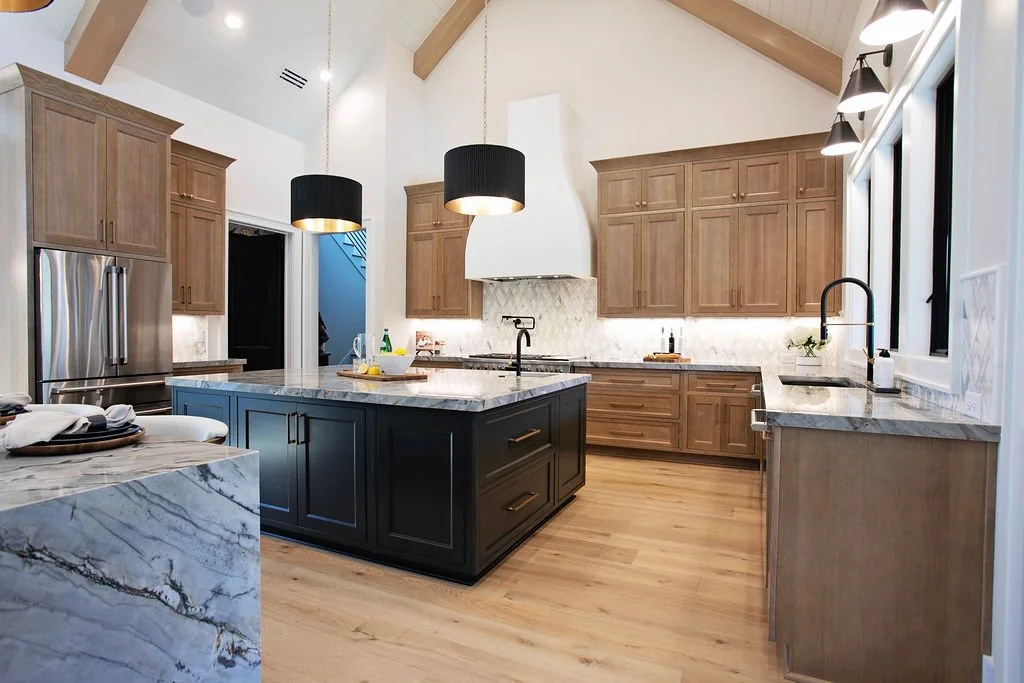 Modern kitchen with wooden cabinets, a black island, marble countertops, and pendant lighting.