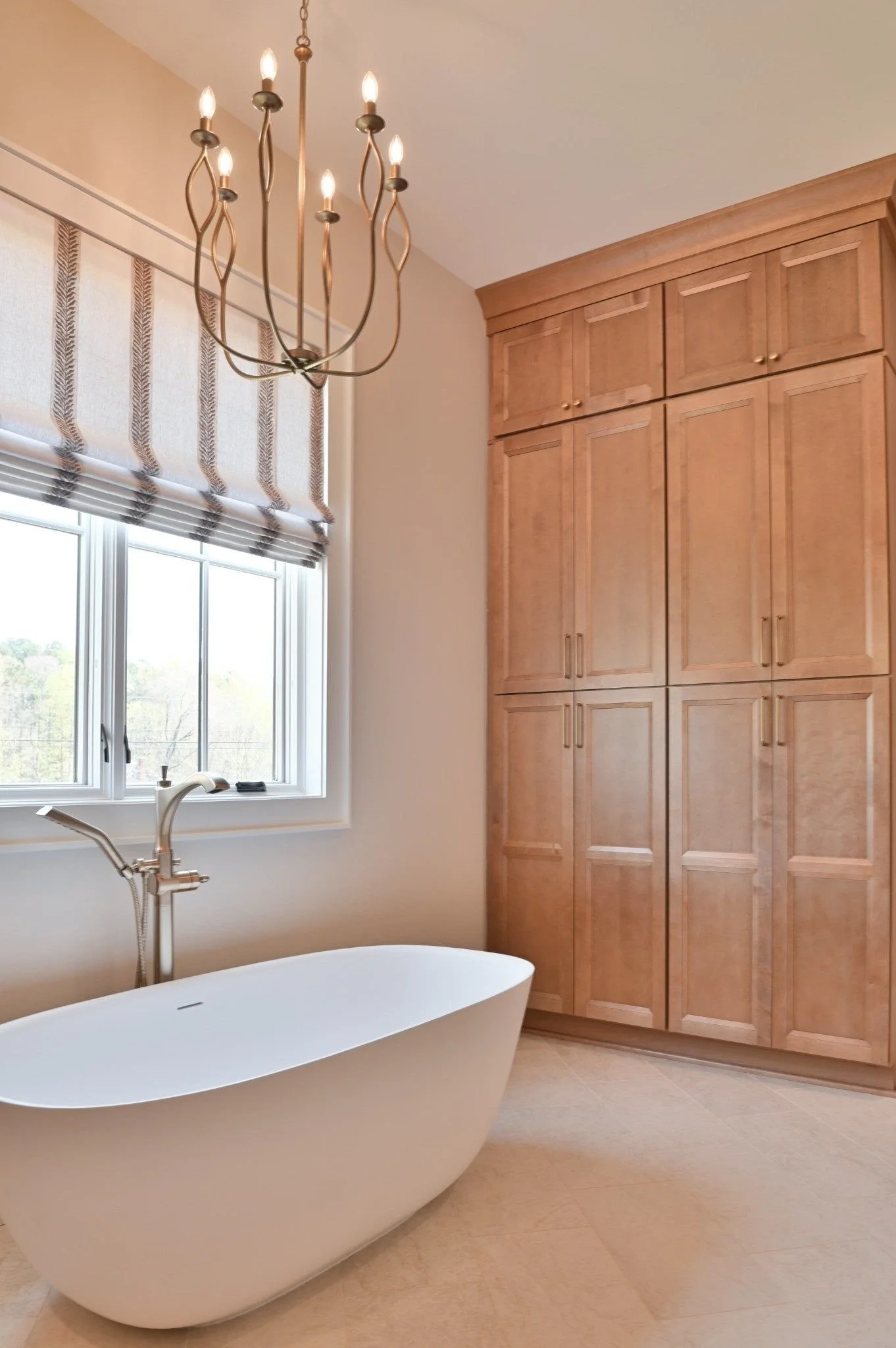 Custom bathroom cabinetry and tile flooring in a luxury Reynolds Lake Oconee home in Greensboro, Georgia. The bathroom features floor-to-ceiling custom wood cabinetry, a freestanding soaking tub, designer chandelier, quartz countertops & tile floors.