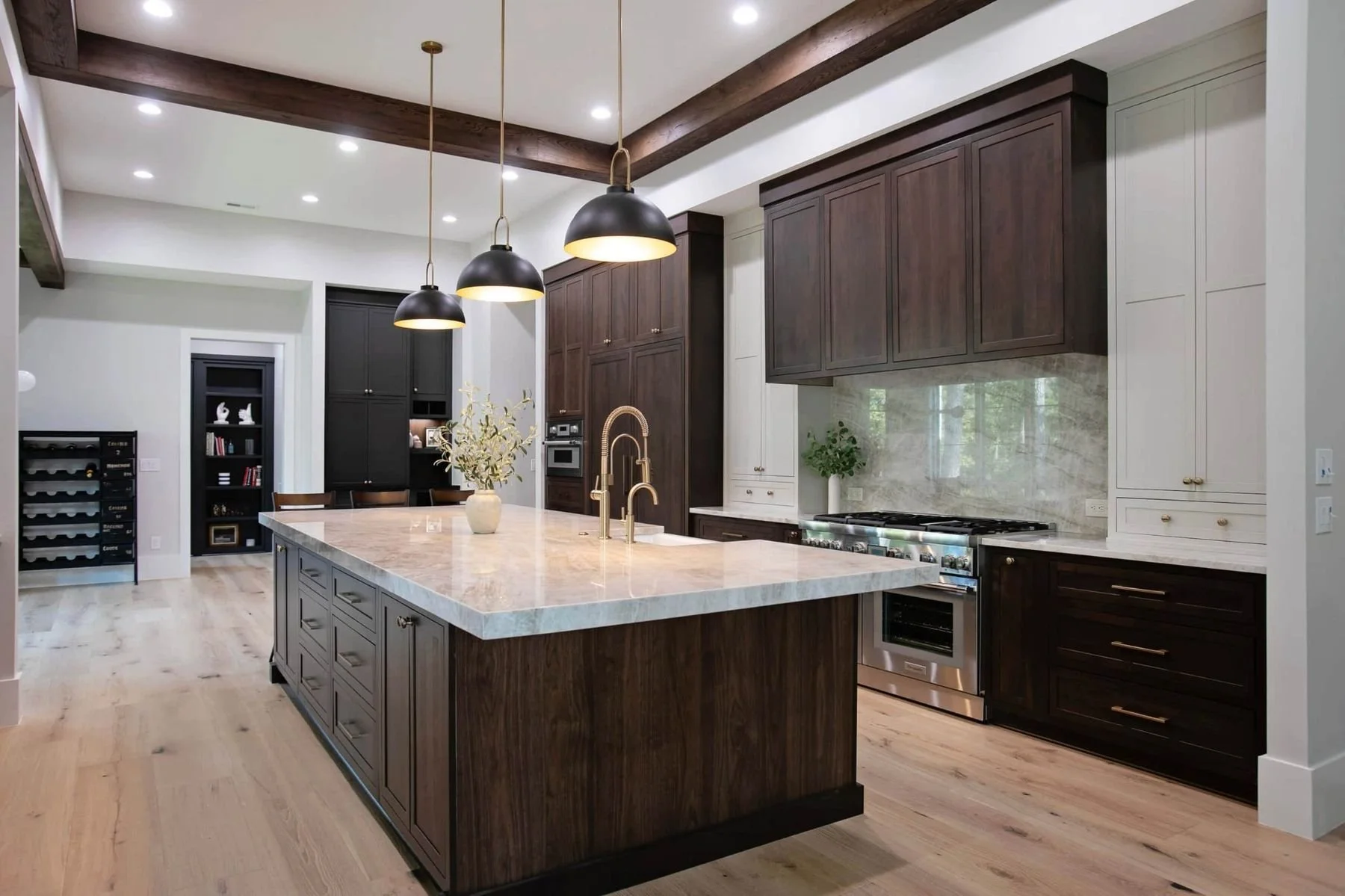 A kitchen with rich stained wood cabinets, a large waterfall-edge island with seating, quartz countertops, decorative pendant lighting, integrated appliance storage, and wide-plank hardwood flooring designed for upscale lakefront living.