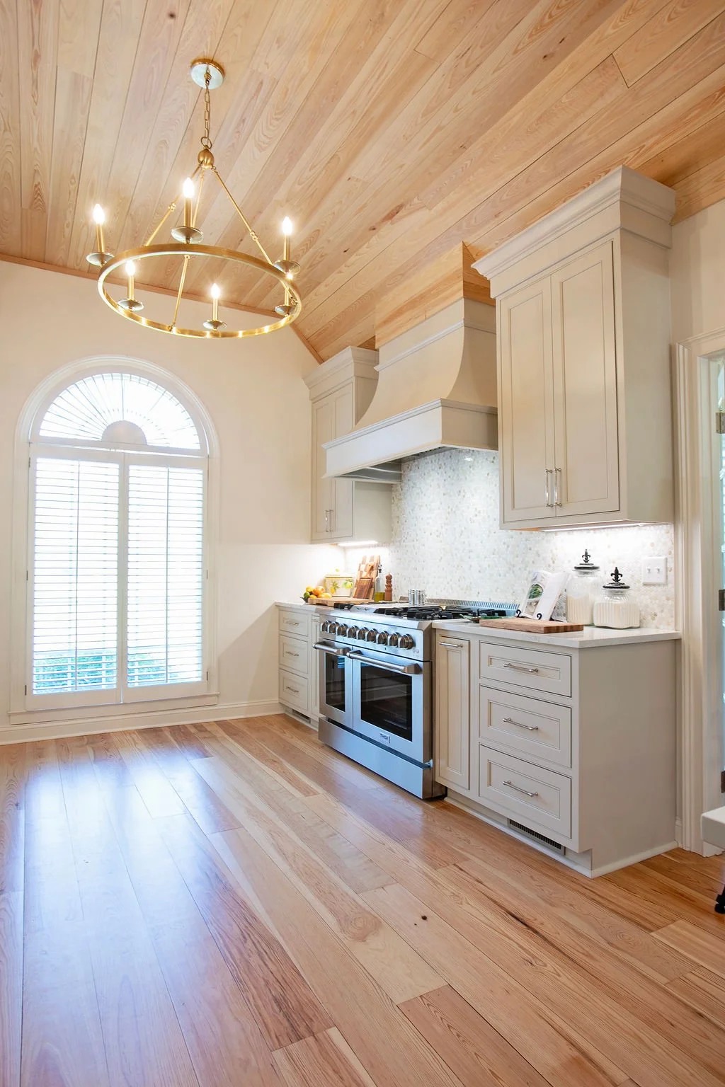 Heart pine hardwood flooring spanning kitchen, dining, and living areas with tongue-and-groove wood ceiling and large circular chandelier creating a warm, cohesive open-concept space