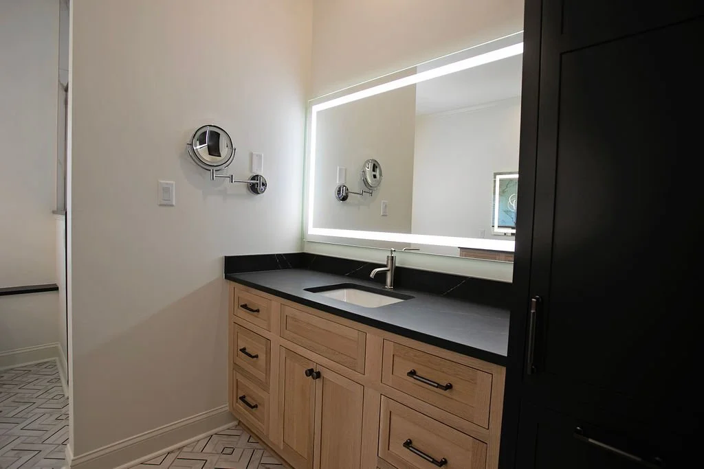 A warm natural wood vanity is paired with a bold black tower cabinet, creating striking contrast while offering a mix of open access and vertical storage for a modern, functional design.