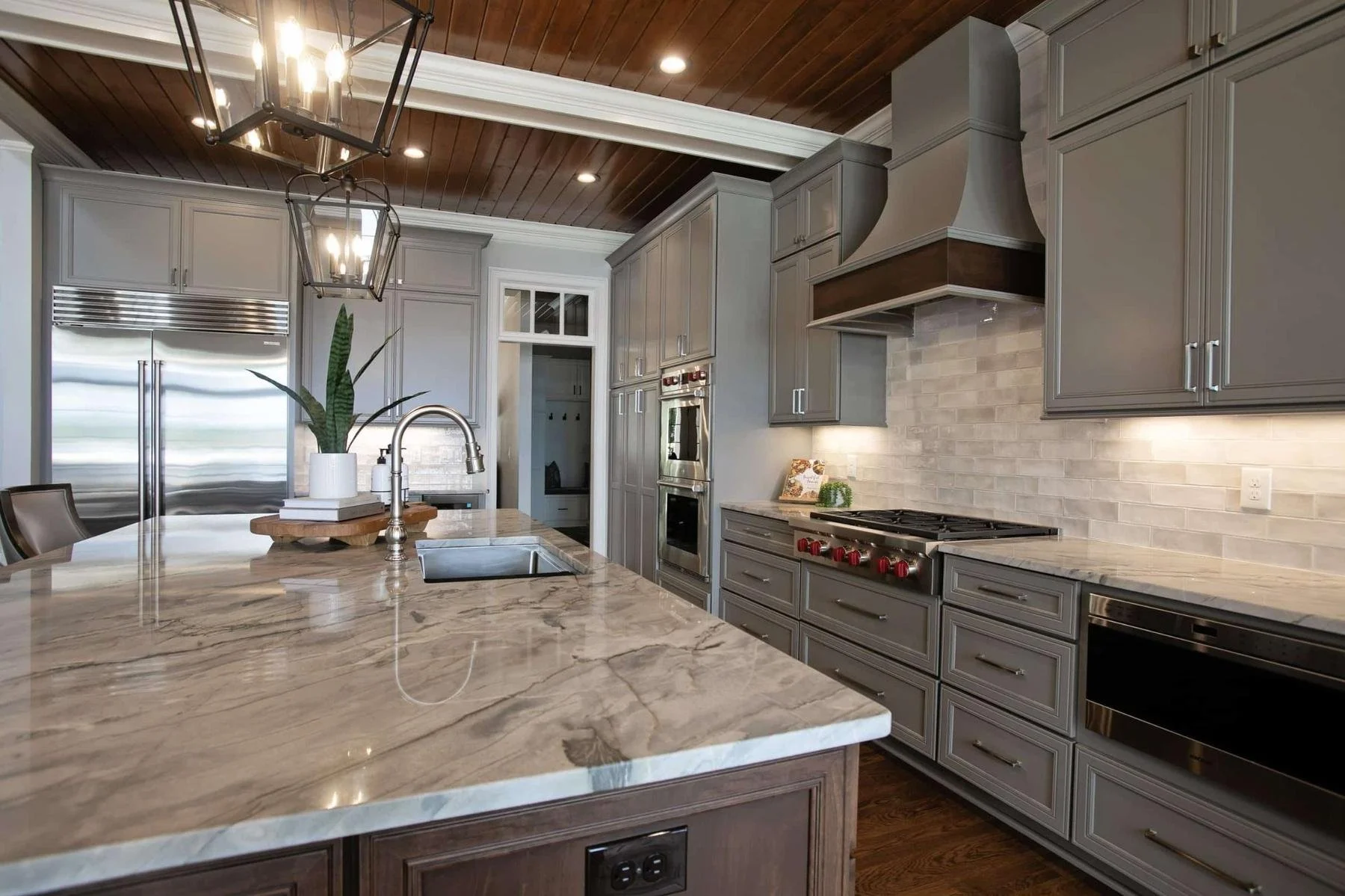 Luxury kitchen with custom gray shaker cabinets, quartz island, stainless range hood, hardwood flooring, and wood ceiling in Reynolds Lake Oconee, Greensboro, GA.