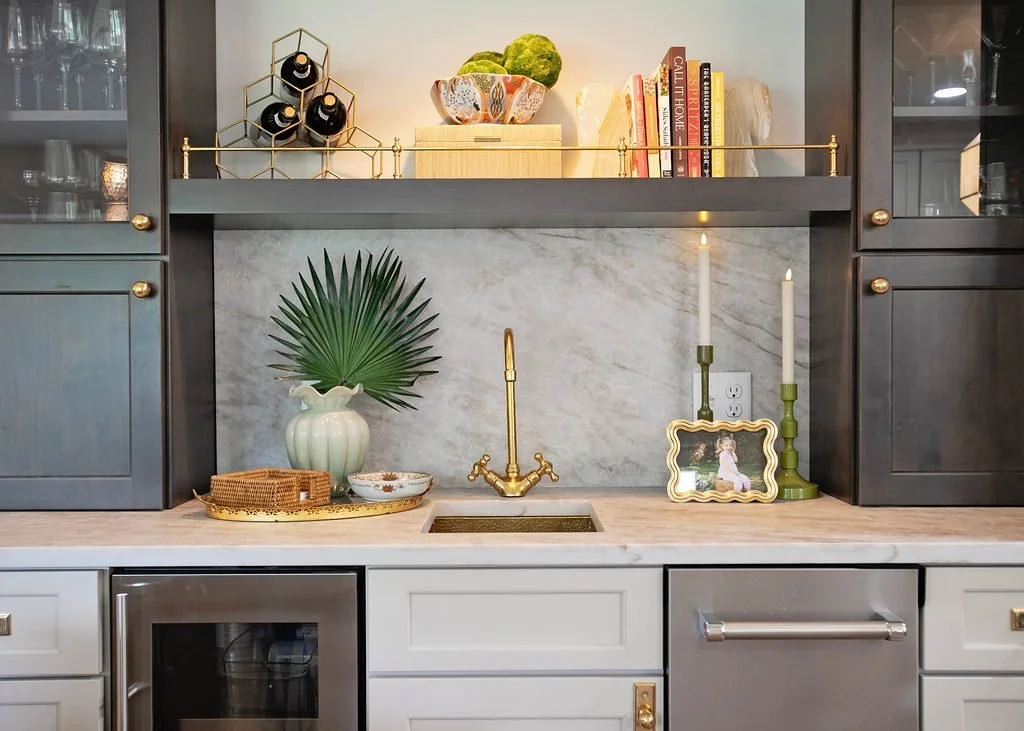 Custom home bar cabinetry featuring painted lower cabinets, dark-stained display towers, open shelving with brass gallery rails, integrated refrigeration, and decorative lighting.